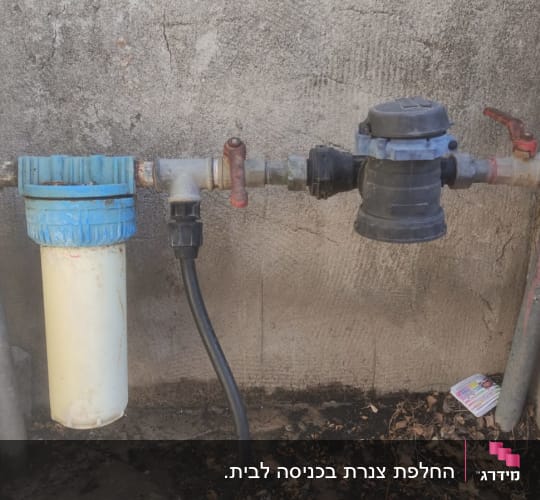 צינורות מים עם מסנן וברזים על קיר בטון.